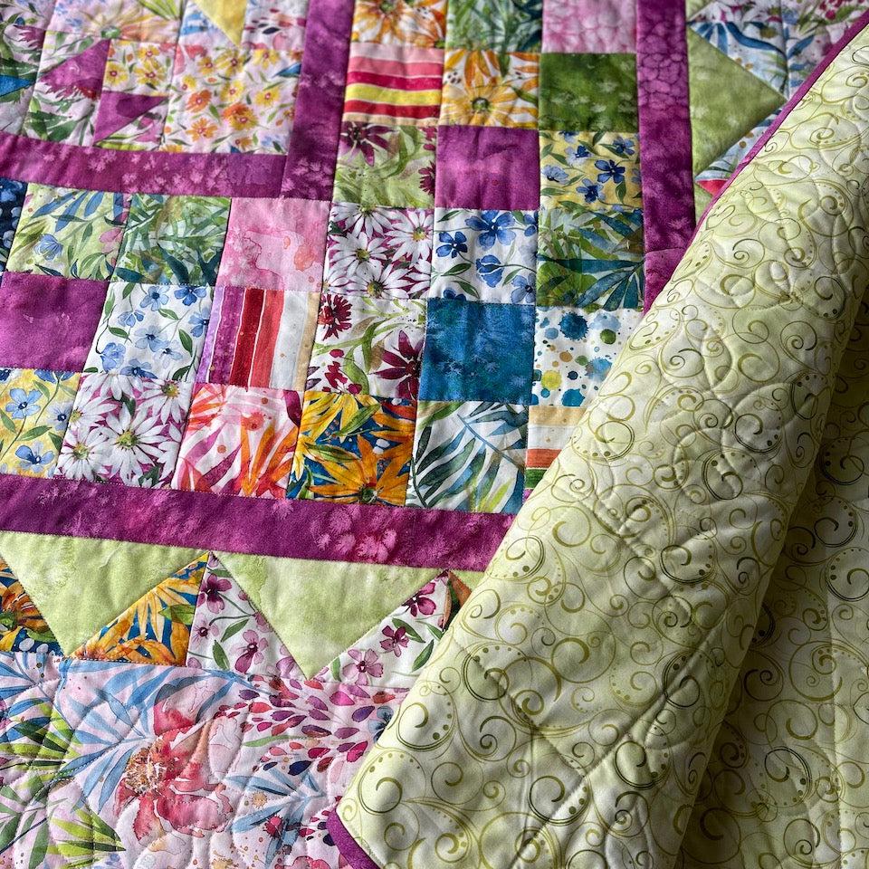 A close up of My Mother's garden quilt showing some of the borders in more detail. a corner of the quilt is turned back so you can see the green quilt backing with a fine scroll print.