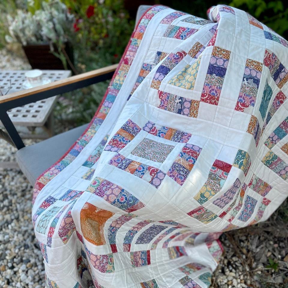 Closeup photo of the Anemone Quilt in the garden, draped over a chair.