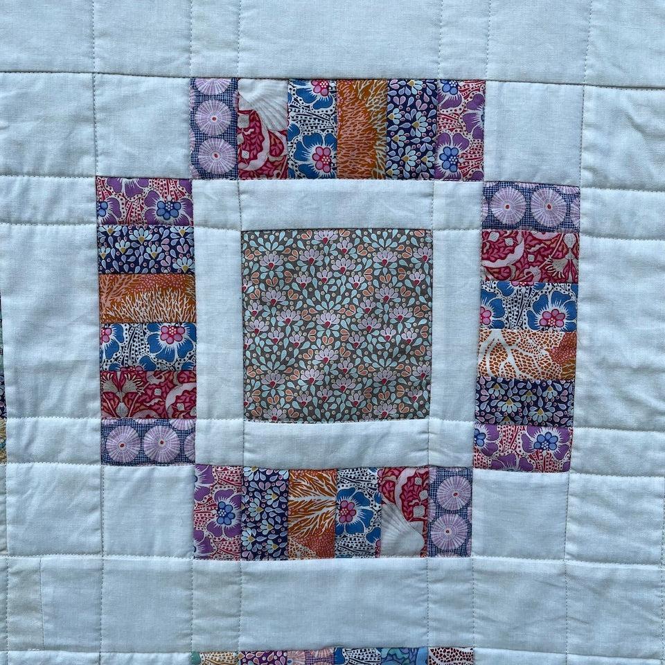 Close up of one of the blocks in the Anemone Quilt.  It shows the centre square with a small sea anemone print surrounded by a small cream border plus a pieced border with a number of different fabrics with a seaside theme.