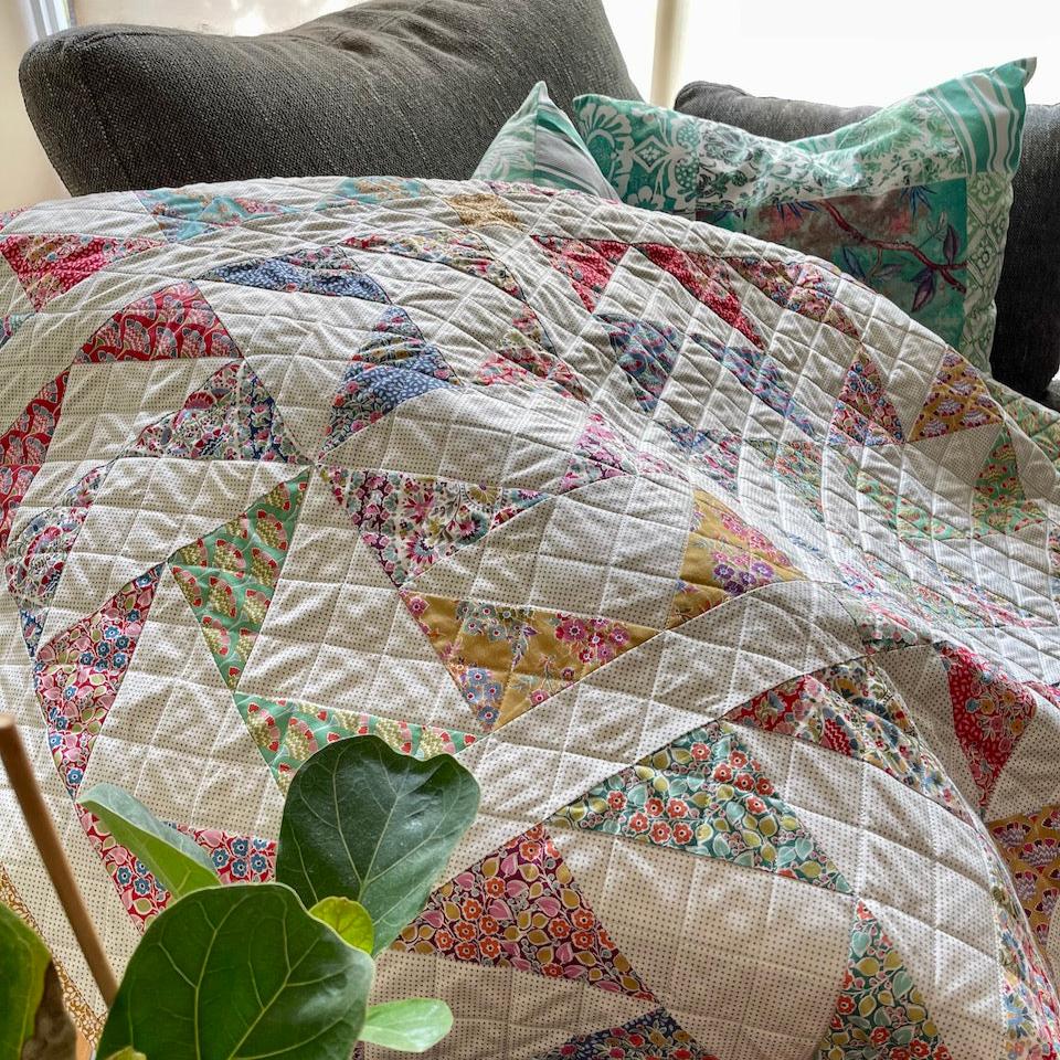 Closeup of the quilt showing the diagonal grid of lines quilted across the quilt. There are leaves of a plant in the foreground.