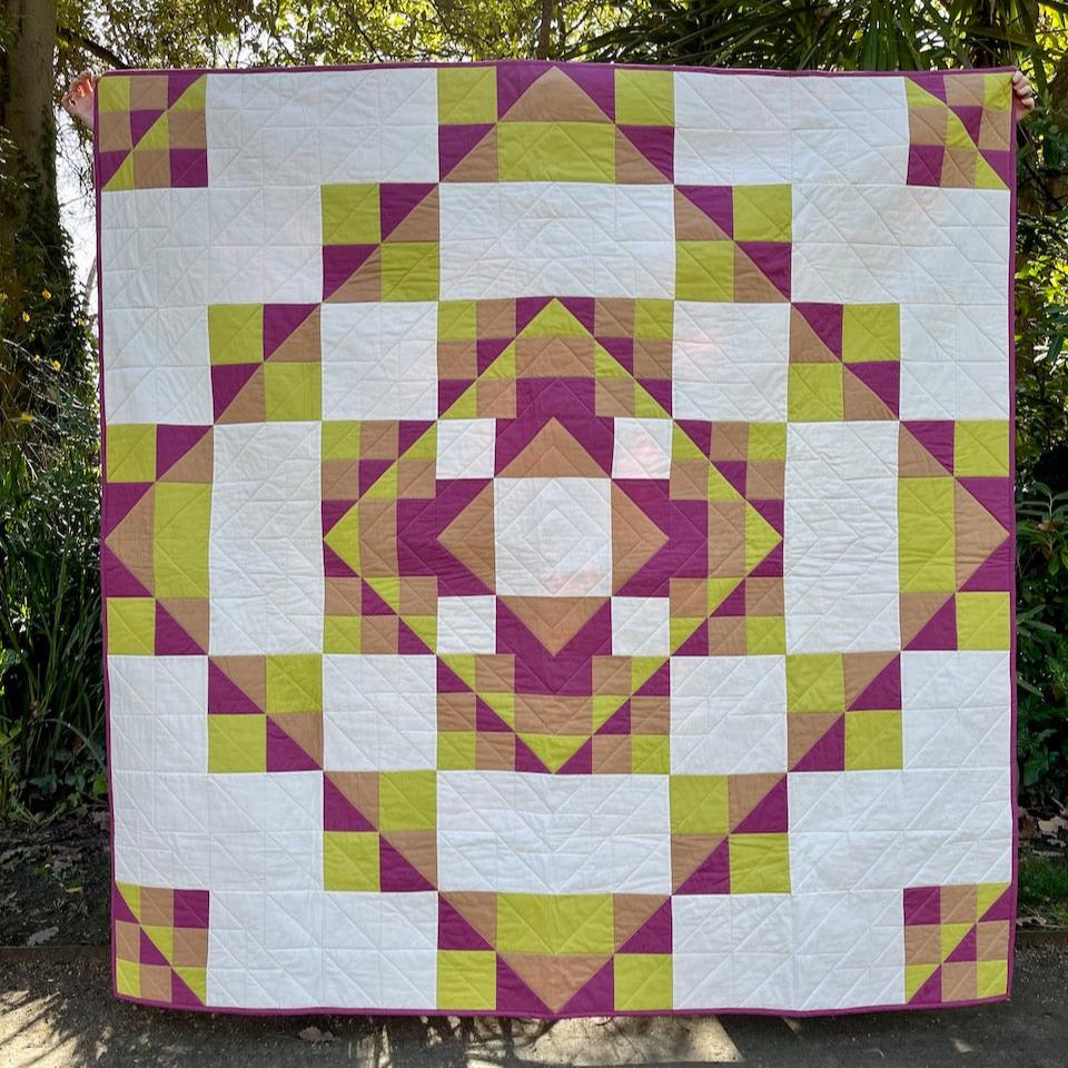 Kaleidoscope Quilt in Full in the garden showing the radiating greens and plum colours of the blocks.