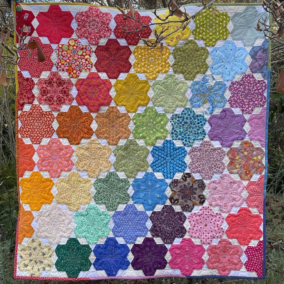 The Little Blooms Quilt hanging in a tree showing the rainbow coloured flowers.