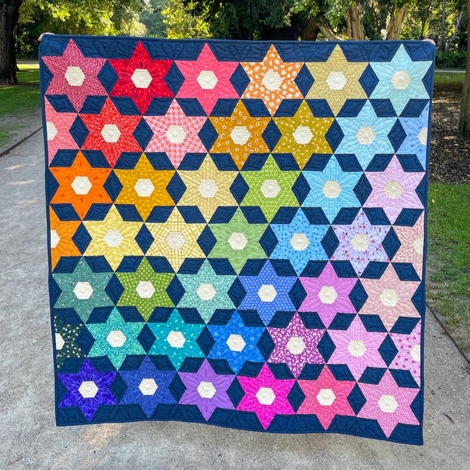 Night Blooms Quilt shown in full showing the rainbow of coloured flowers against a dark blue background.