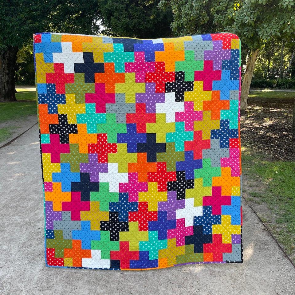 The colourful Plus Quilt shown in full along a garden path