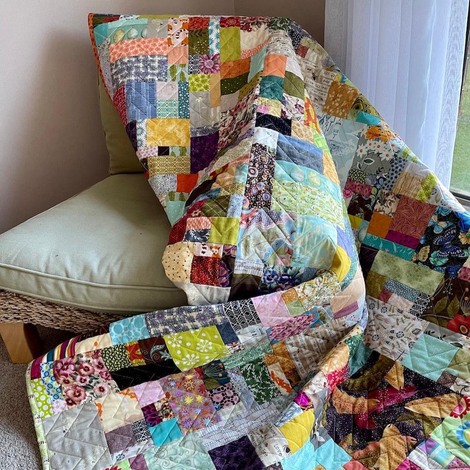 The Scrap Quilt draped over a chair showing a close up of the quilt