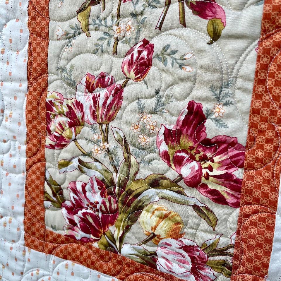 Close up of a rectangular block showing the tulip fabric in greens , pinks and yellow surrounded by an orange border.