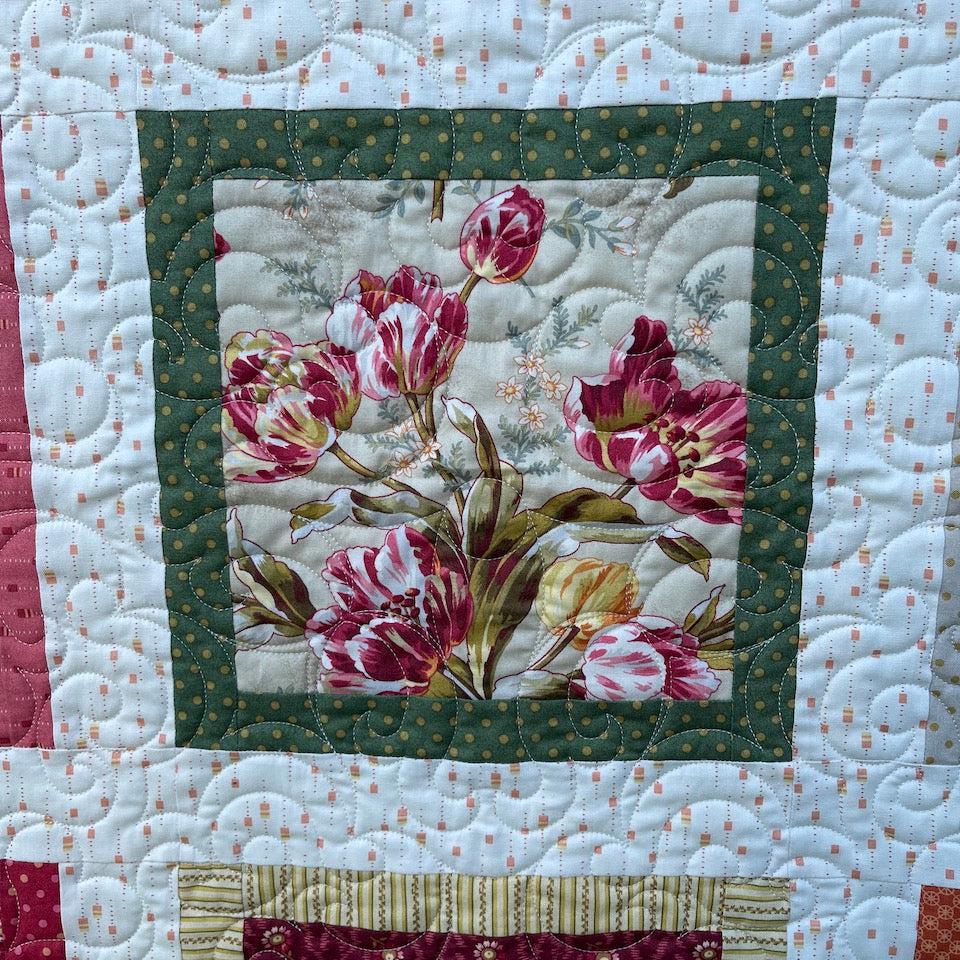 Close up of a square block showing the tulip fabric in greens , pinks and yellow surrounded by an green border.